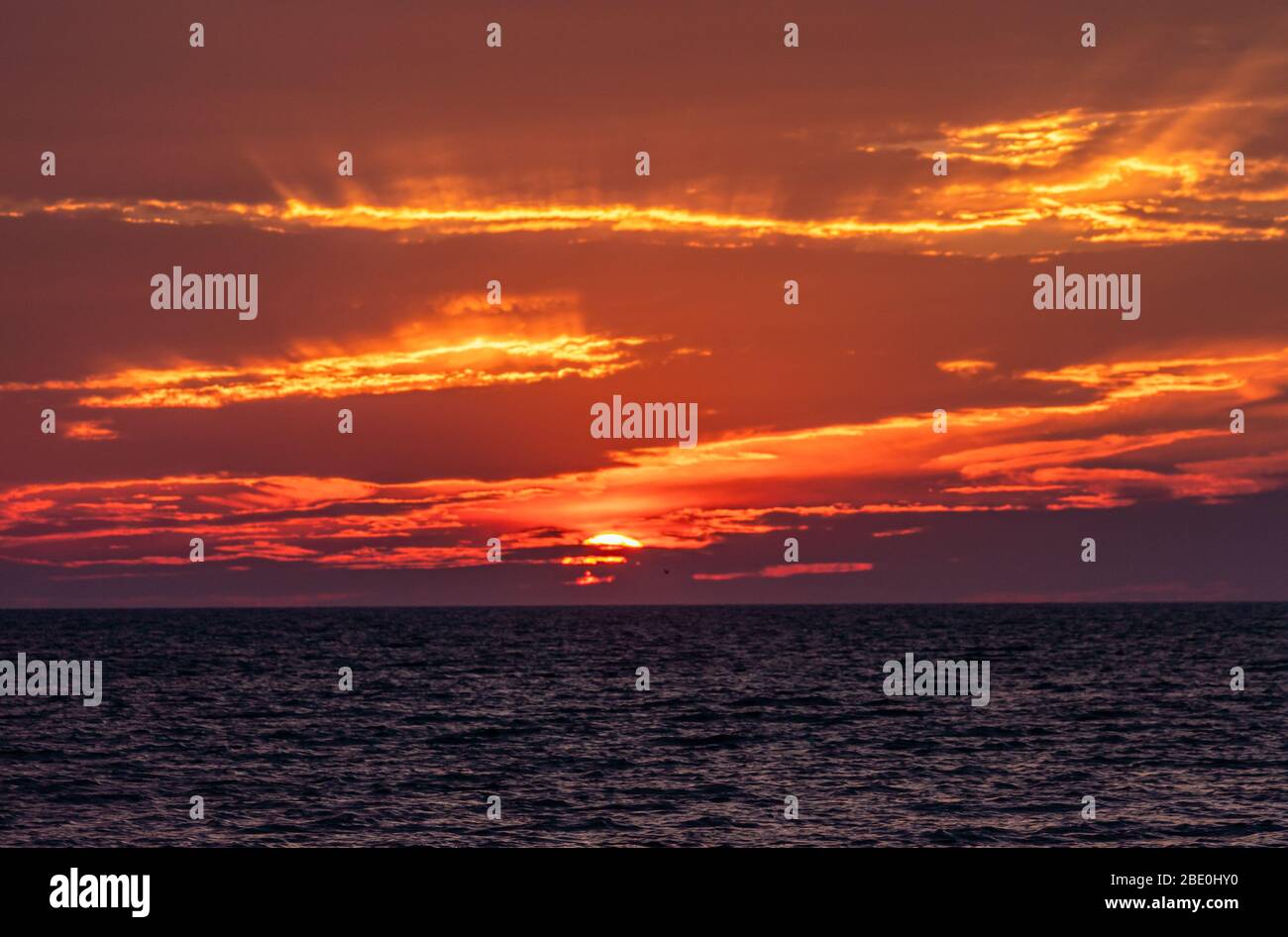 Sun setting at ocean horizon as sky catches fire. Stock Photo