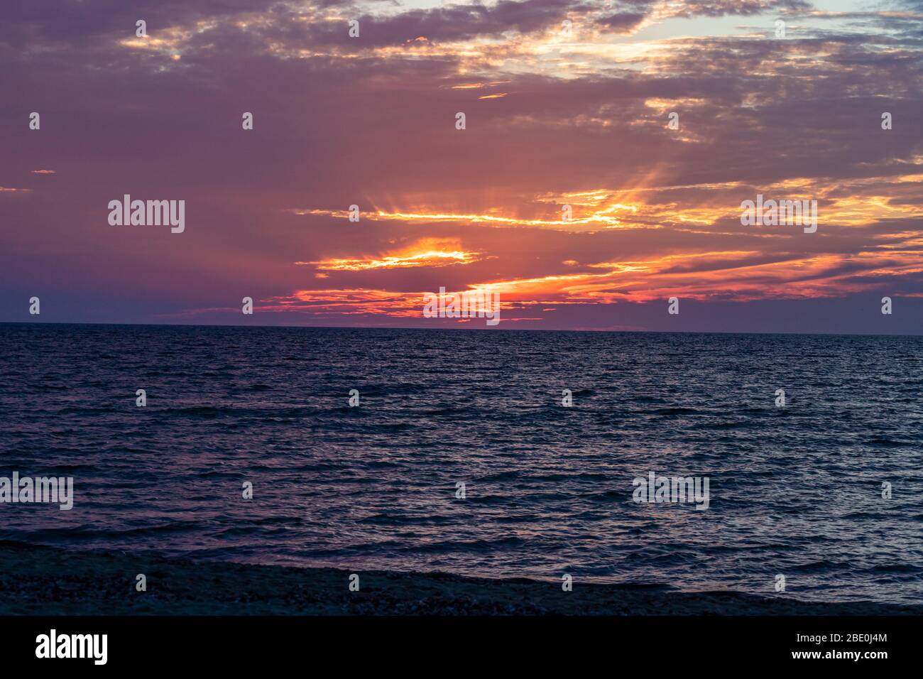 Sun rays shining through clouds as the sun sets along ocean horizon. Stock Photo