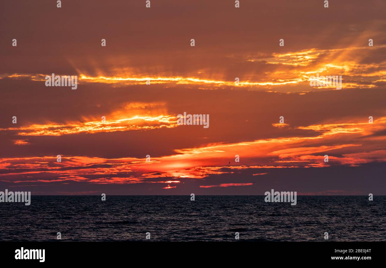 Light rays shining through clouds as the sun sets at ocean horizon. Stock Photo