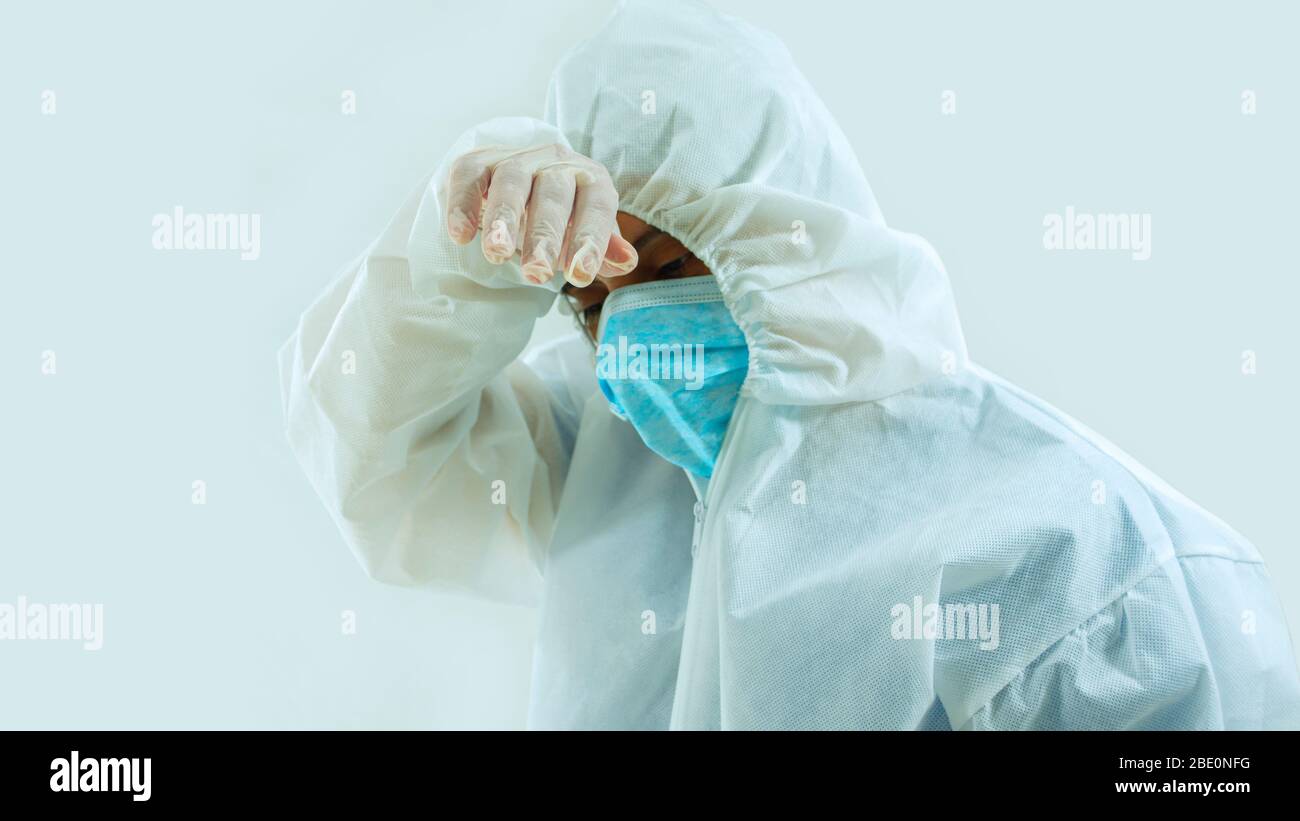 Front view of doctor with blue mask and bioprotective suit with hand on forehead with tiredness, sadness or worry attitude on white background Stock Photo