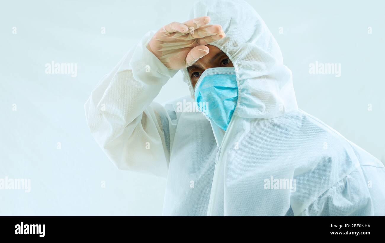 Front view of doctor with blue mask and bioprotective suit with hand on forehead with tiredness, sadness or worry attitude on white background Stock Photo