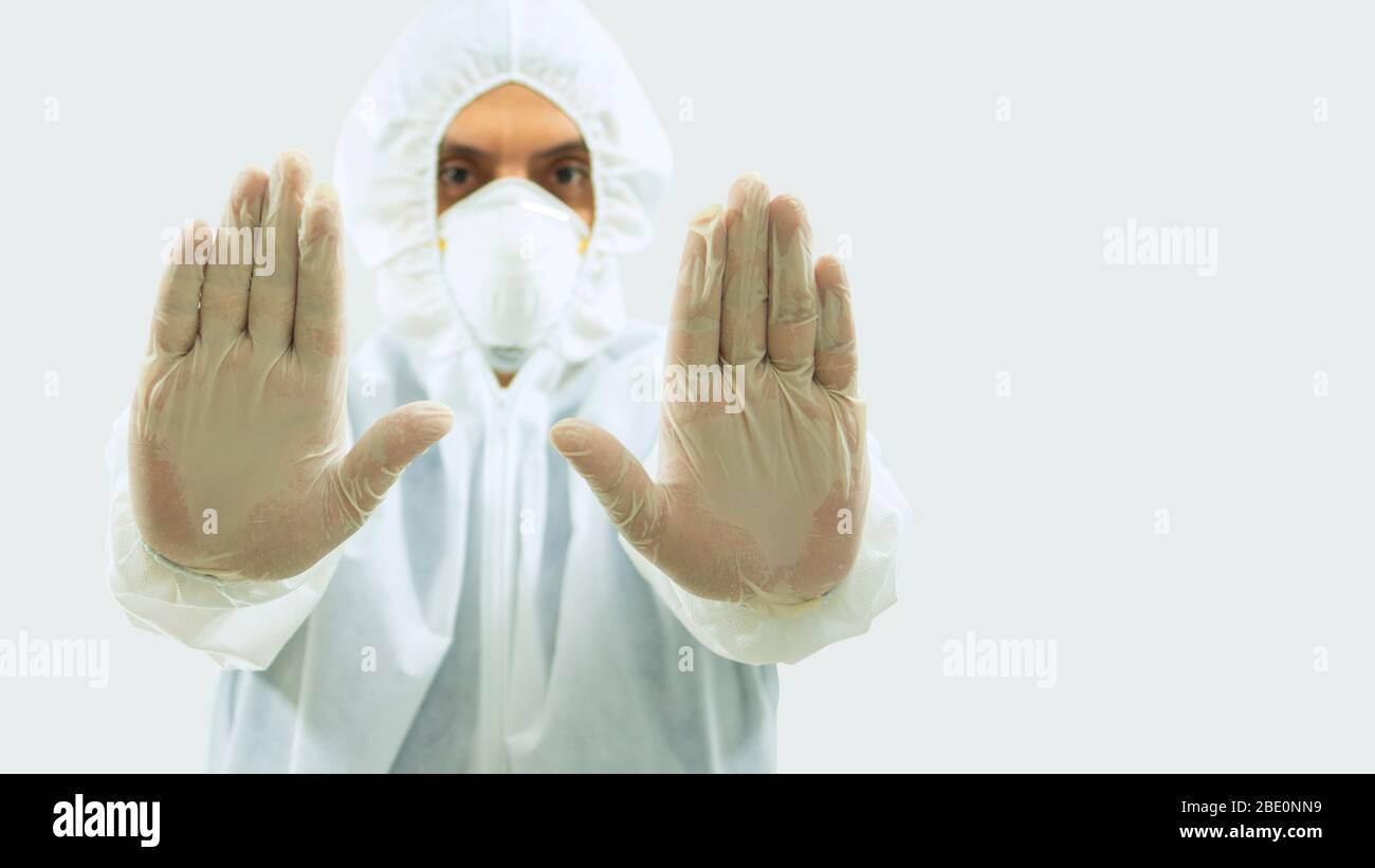 Front view of doctor with mask and bioprotective suit with arms outstretched forward and his open hands making a stop sign on white background Stock Photo