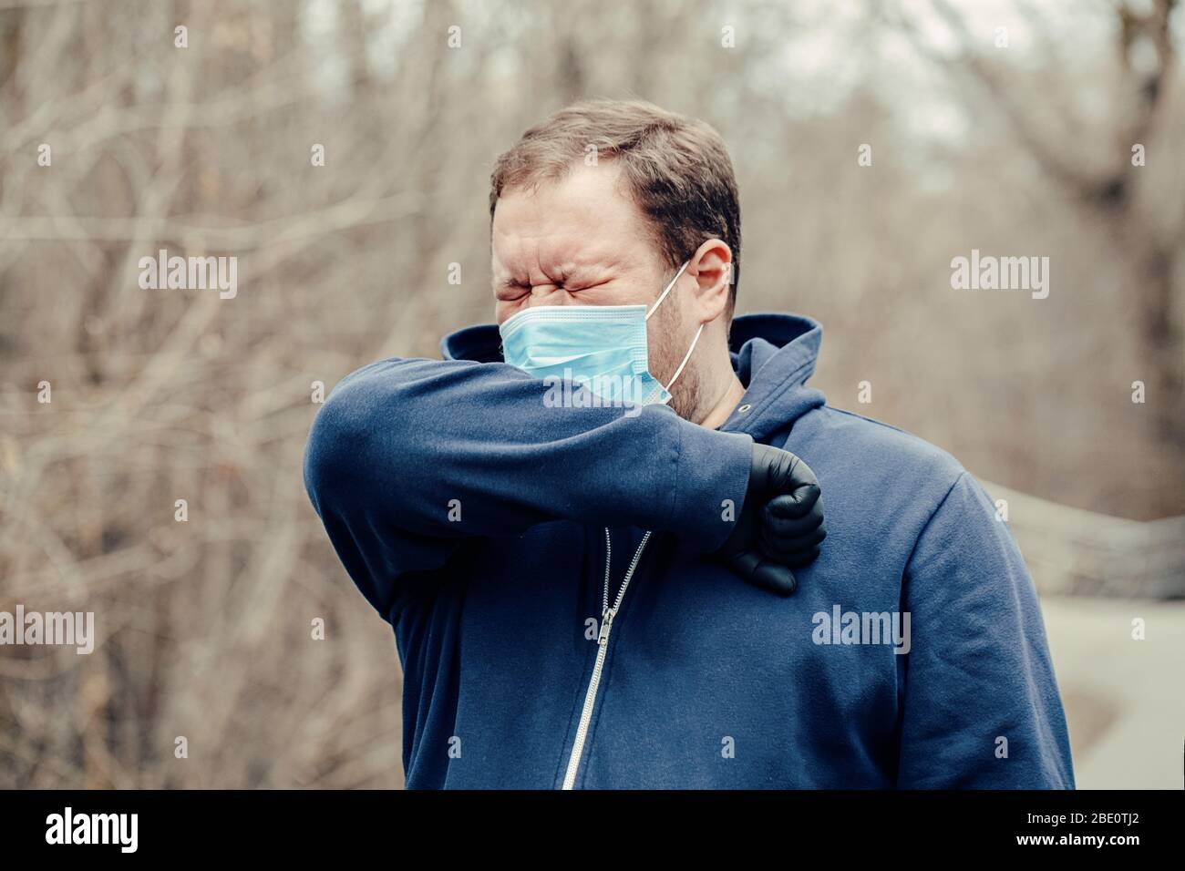 Caucasian young middle age man in sanitary face mask sneezing coughing outdoor. Person protecting from dangerous spread of virus. Coronavirus COVID-19 Stock Photo