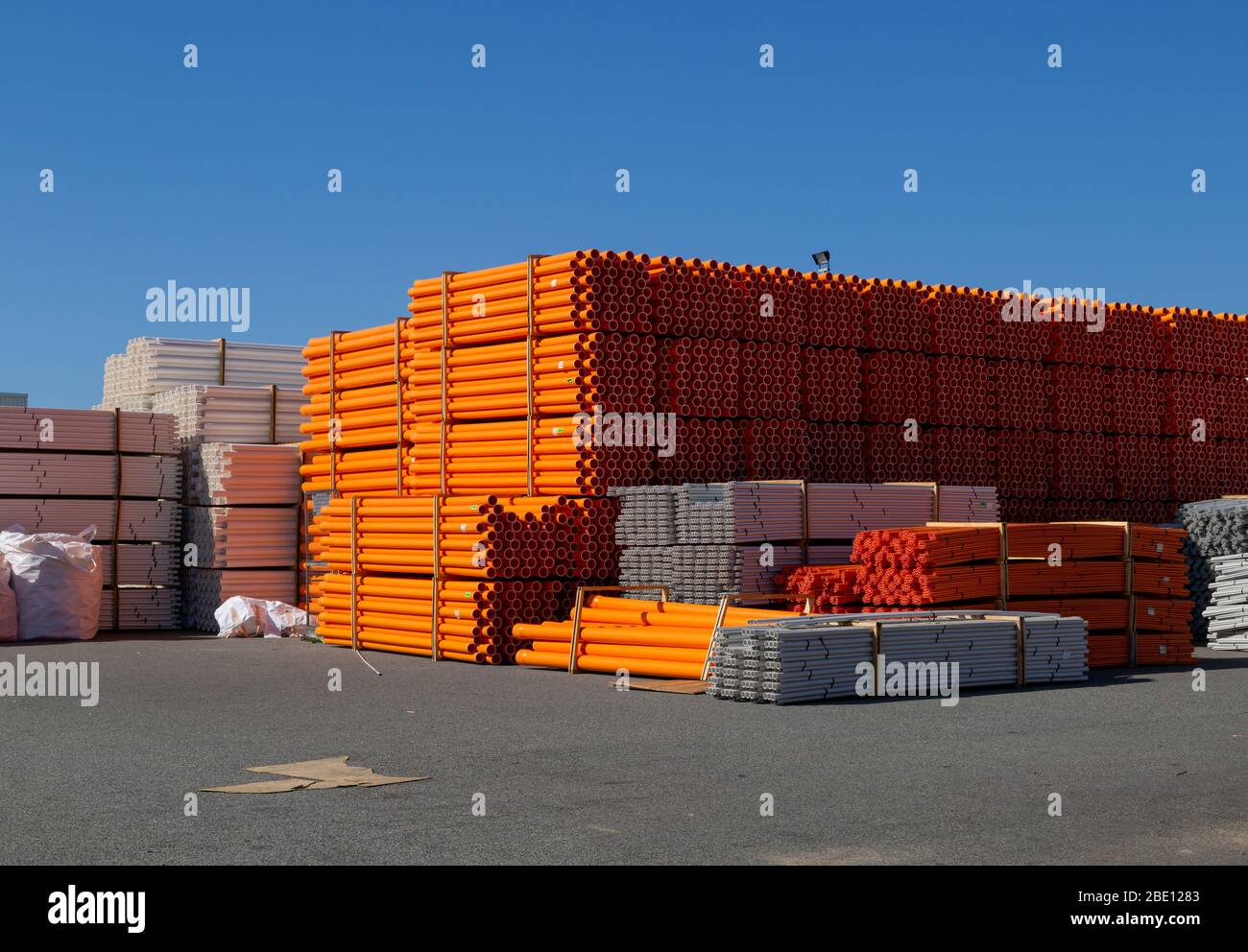 Orange and white plastic pipes stacked in an industrial storage yard