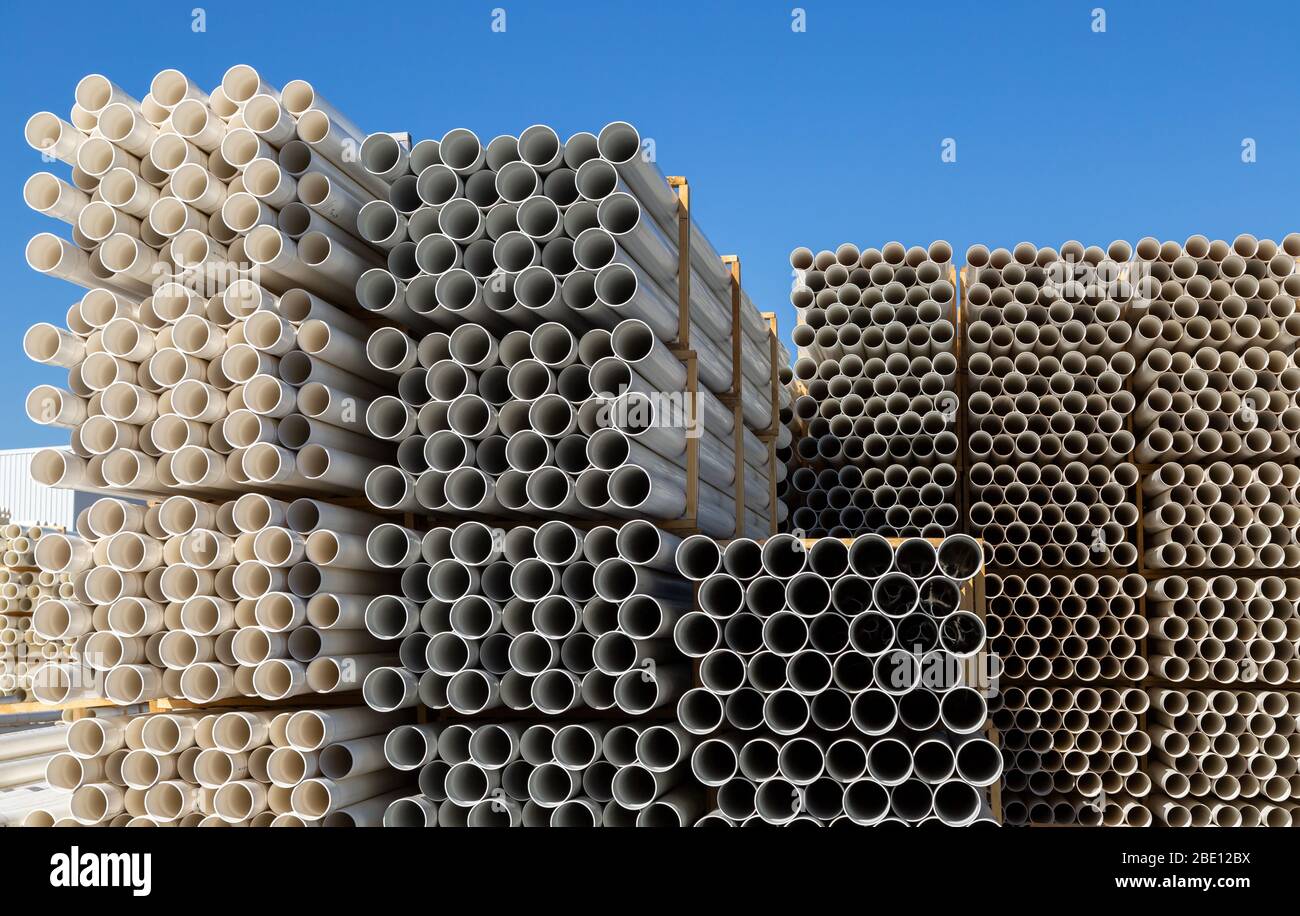 White plastic pipes stacked outside in an industrial yard with blue sky background Stock Photo