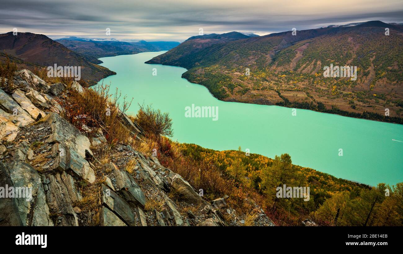 Crescent shaped, milky green colored Kanas lake surrounded by Altay mountain ranges with autumn foliage. Stock Photo