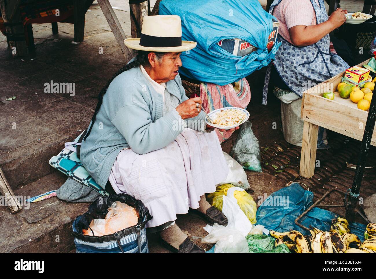 Pisac, Peru - July 29 2010: Local Elderly Woman Eating Noodles on an Indio Market in Peru Wearing a Straw Hat. Stock Photo