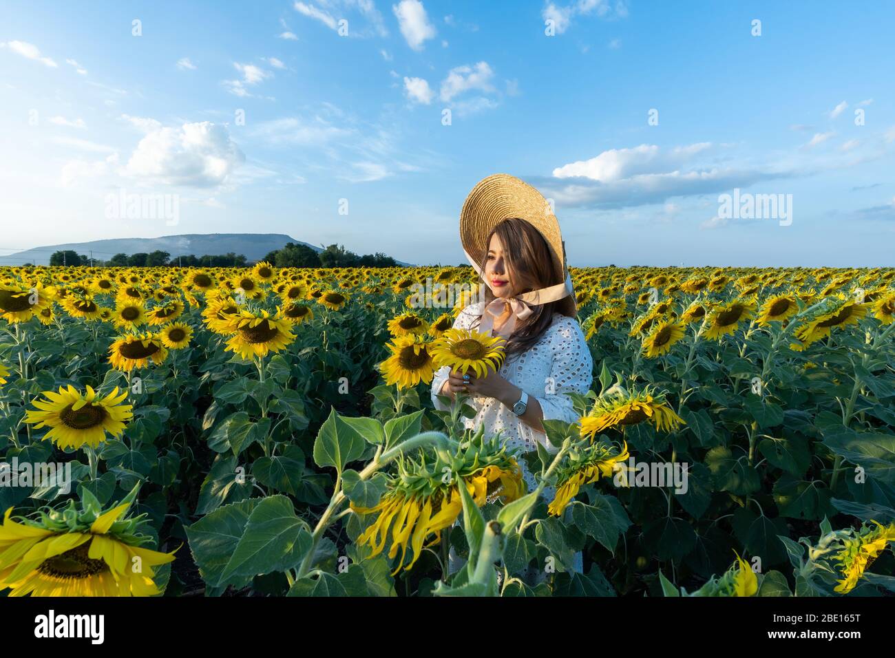 A beautiful asian women in a white dress and hat walking on a field of ...
