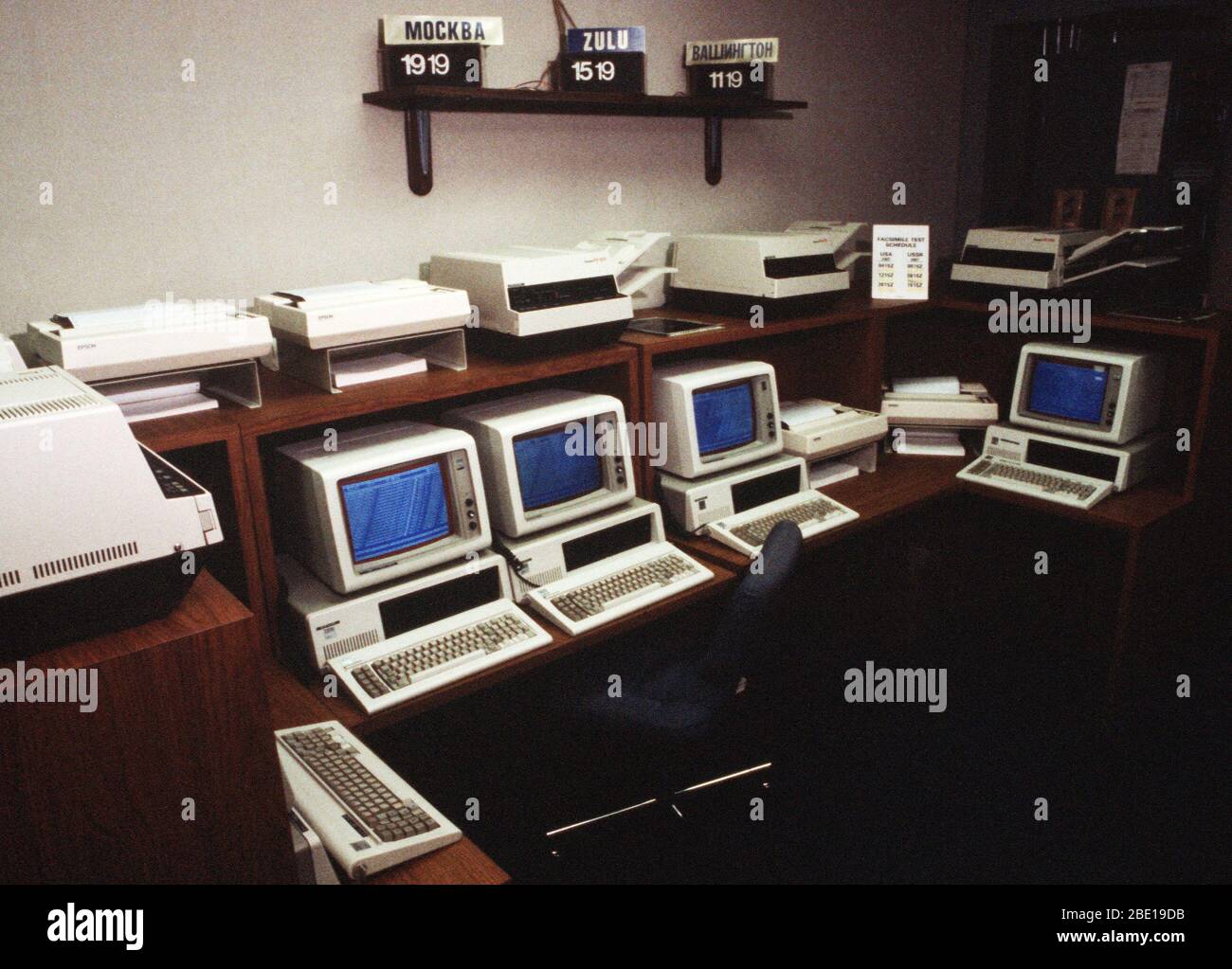 A view of computer stations, printers and facsimile machines that are part of American terminus of the Washington-Moscow Direct Communications Link.  Clocks on the wall give Moscow, Greenwich Mean (Zulu) and local times; a regular facsimile machine test schedule is at right. Stock Photo