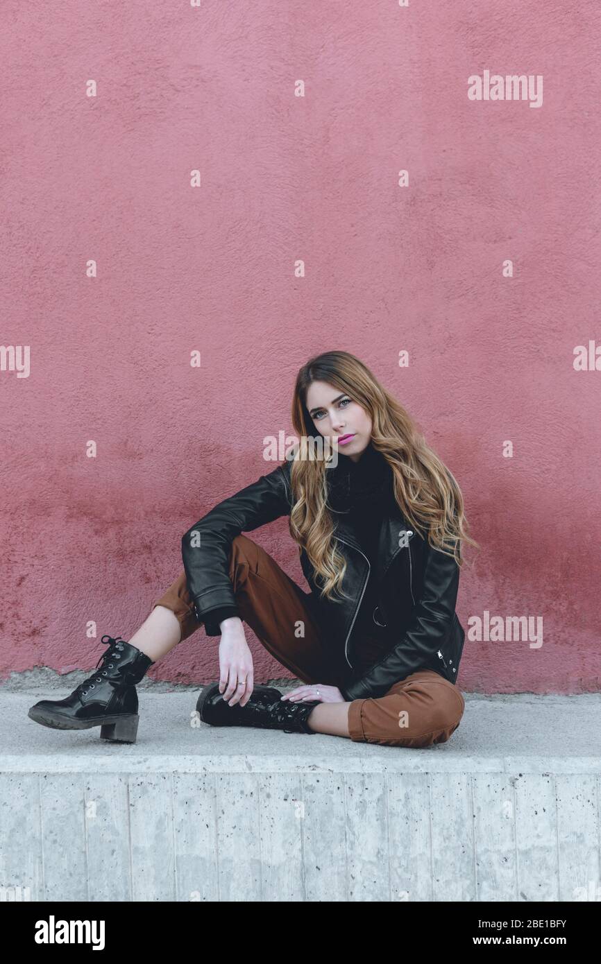 Young professional female model wearing urban clothing for fall collection posing sitting on a street photoshoot for her modeling portfolio Stock Photo