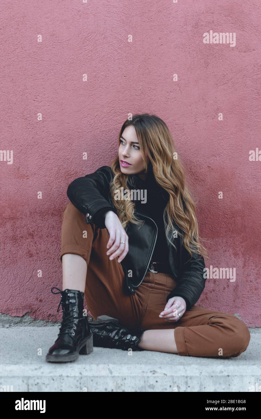 Young professional female model wearing urban clothing for fall collection posing sitting on a street photoshoot for her modeling portfolio Stock Photo