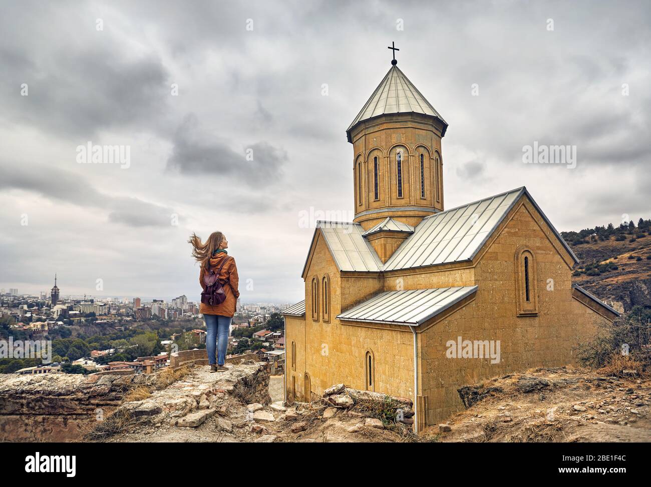Tourist woman near Cathedral in Old medieval castle Narikala at overcast cloudy sky in Tbilisi, Georgia Stock Photo