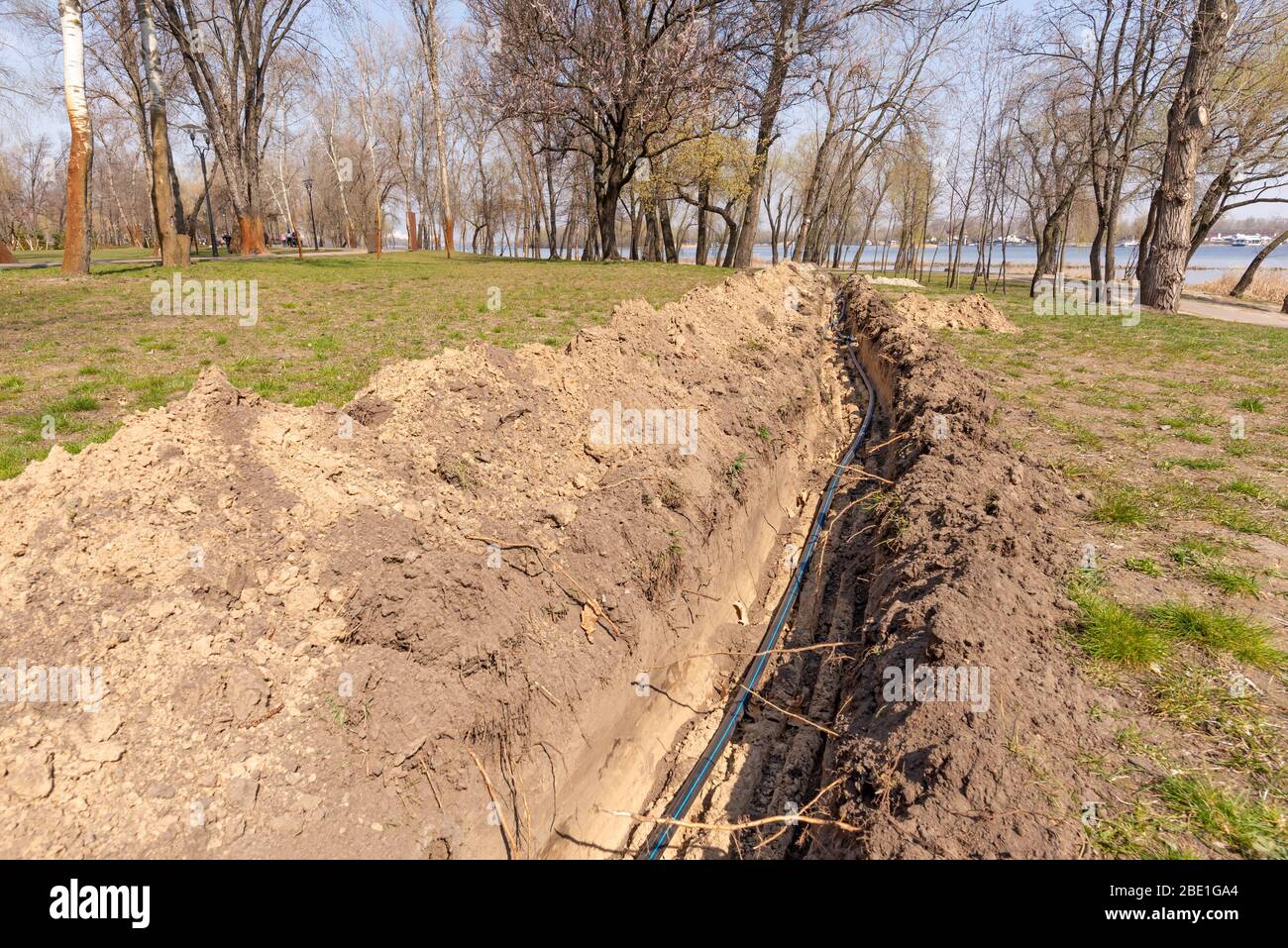 Installation of tubes for an irrigation system in the ground under the trees close to the river. Watering system in the Natalka park of Kiev, Ukraine Stock Photo