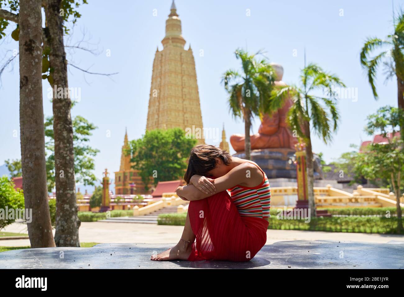 Girl leans on knees, sad, sitting temple Stock Photo