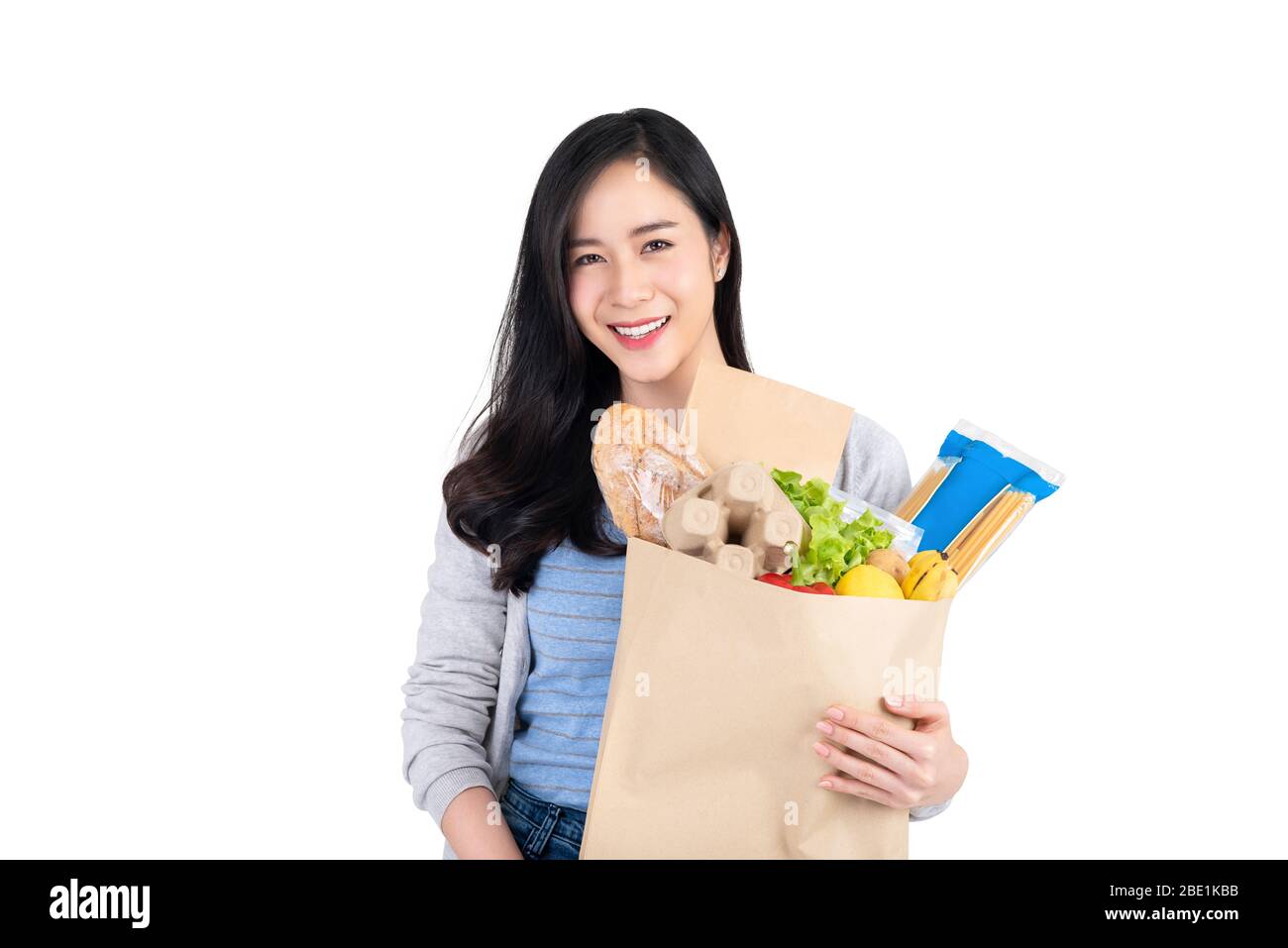 Beautiful smiling Asian woman holding paper shopping bag full of food and groceries isolated on white background Stock Photo
