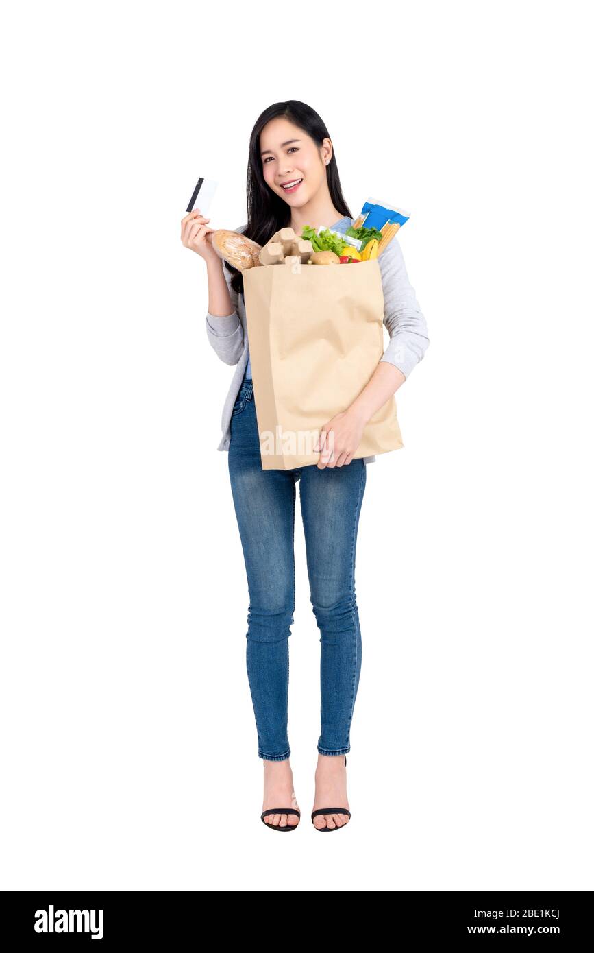 Full length of beautiful Asian woman with credit card holding paper shopping bag full of groceries isolated on studio white background Stock Photo