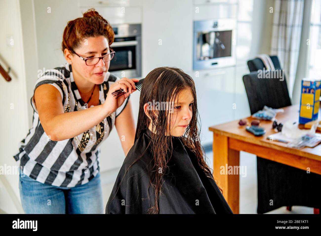 A mother makes her daughters hair at home as all barbershops were ordered to close in an attempt to prevent the spread of coronavirus (COVID-19). Stock Photo