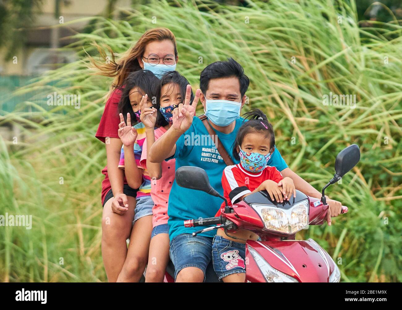 A Thai family travelling on a motorcycle, all wearing protective face masks, taken at Pathumthani, Thailand, in April, 2020. Stock Photo