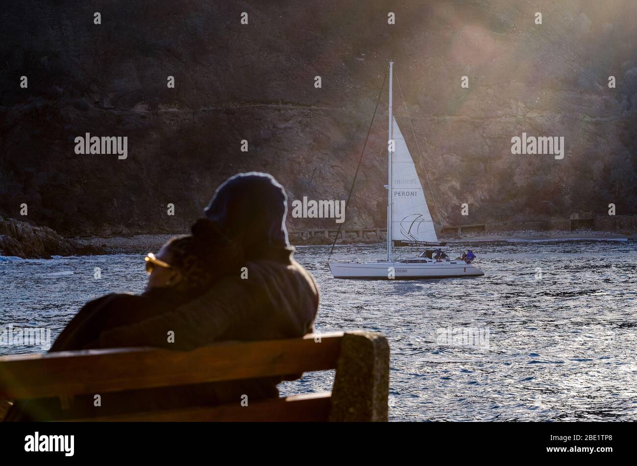 Rear view shot of African couple sitting watching a yacht sail out to sea near sunset Knysna Heads South Africa Stock Photo