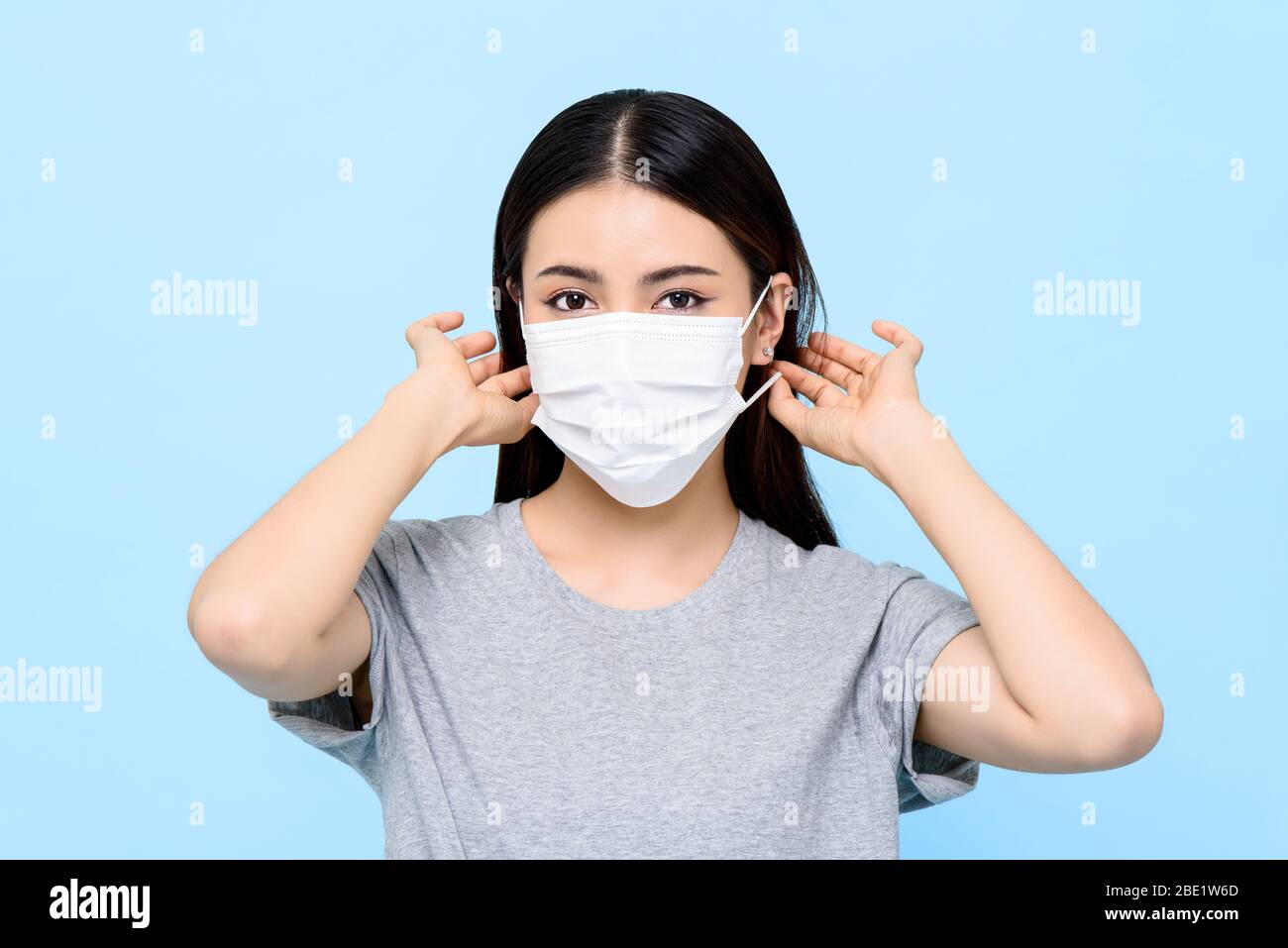 Asian woman wearing medical face mask isolated on light blue background Stock Photo