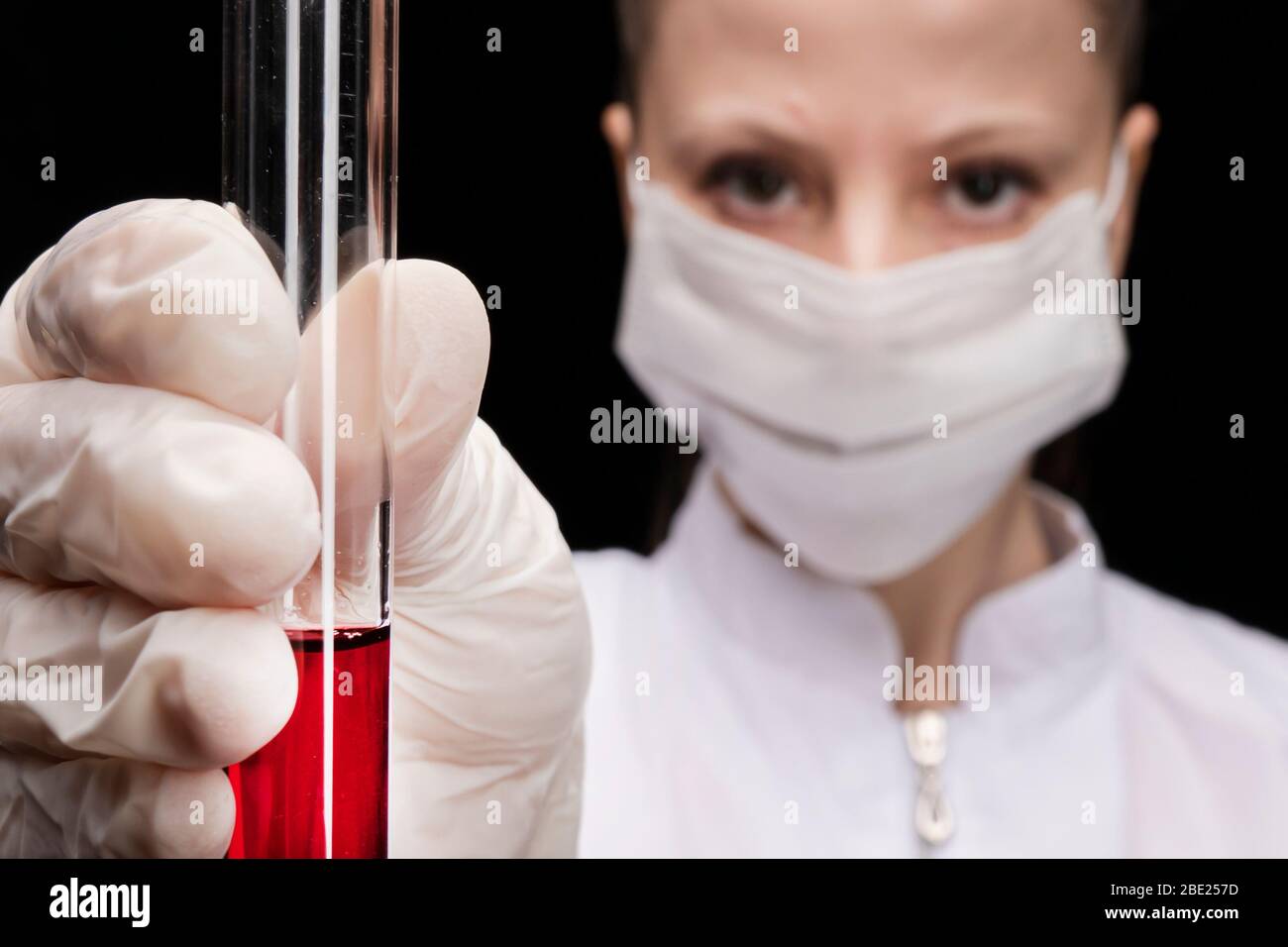 a test tube with a red blood test in the hands of a medical worker in a medical mask. girl doctor in blur. close-up, look. Stock Photo