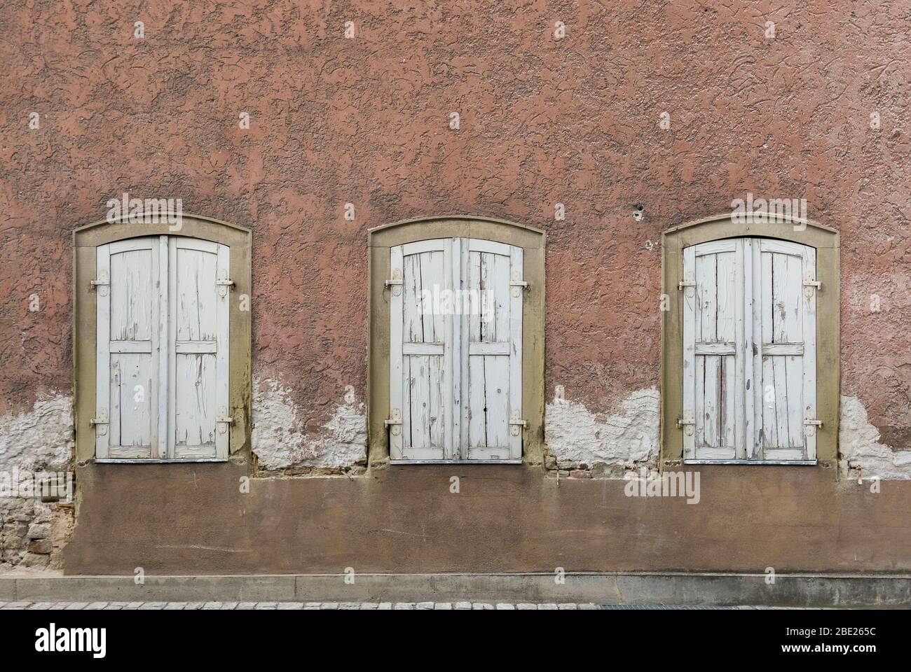 Symmetrical facade of abandoned, dilapidated house with 3 windows with shutters Stock Photo