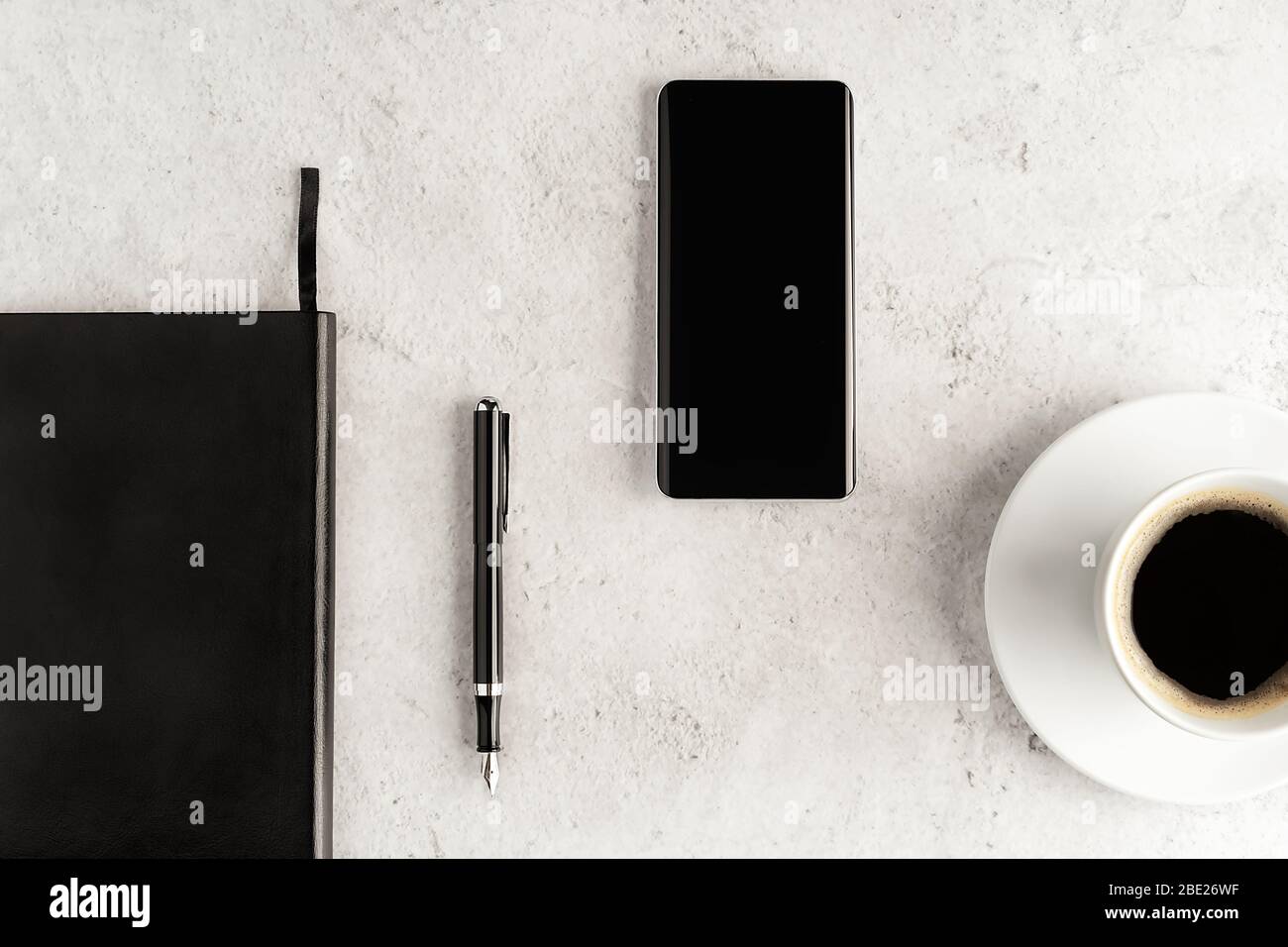 Up-to-date smartphone with notebook, fountain pen and cup of coffee on concrete background. Workstation concept flat lay. Coffee break top view. Mocku Stock Photo