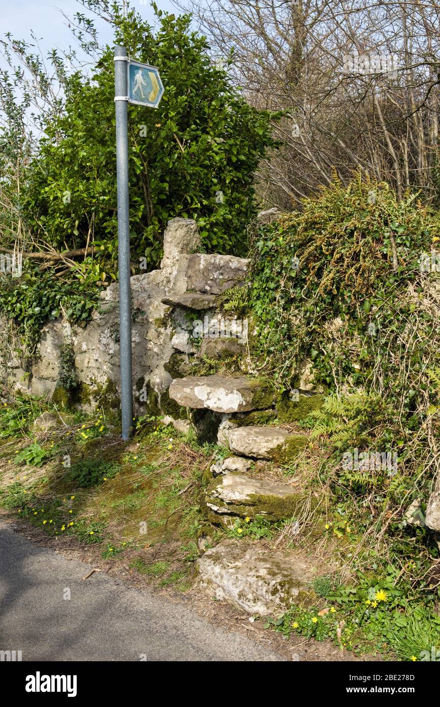 Footpath signpost by quaint old stone stile steps over a wall on a country lane near Benllech, Isle of Anglesey, Wales, UK, Britain Stock Photo