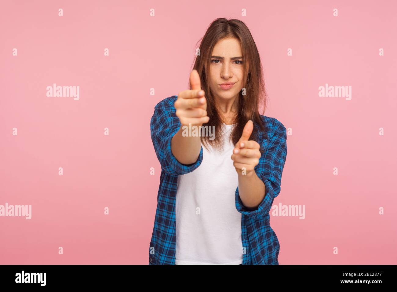 I'll shoot you! Portrait of dangerous girl in checkered shirt pointing finger guns to camera, gesturing weapon and killing, making shot right on targe Stock Photo