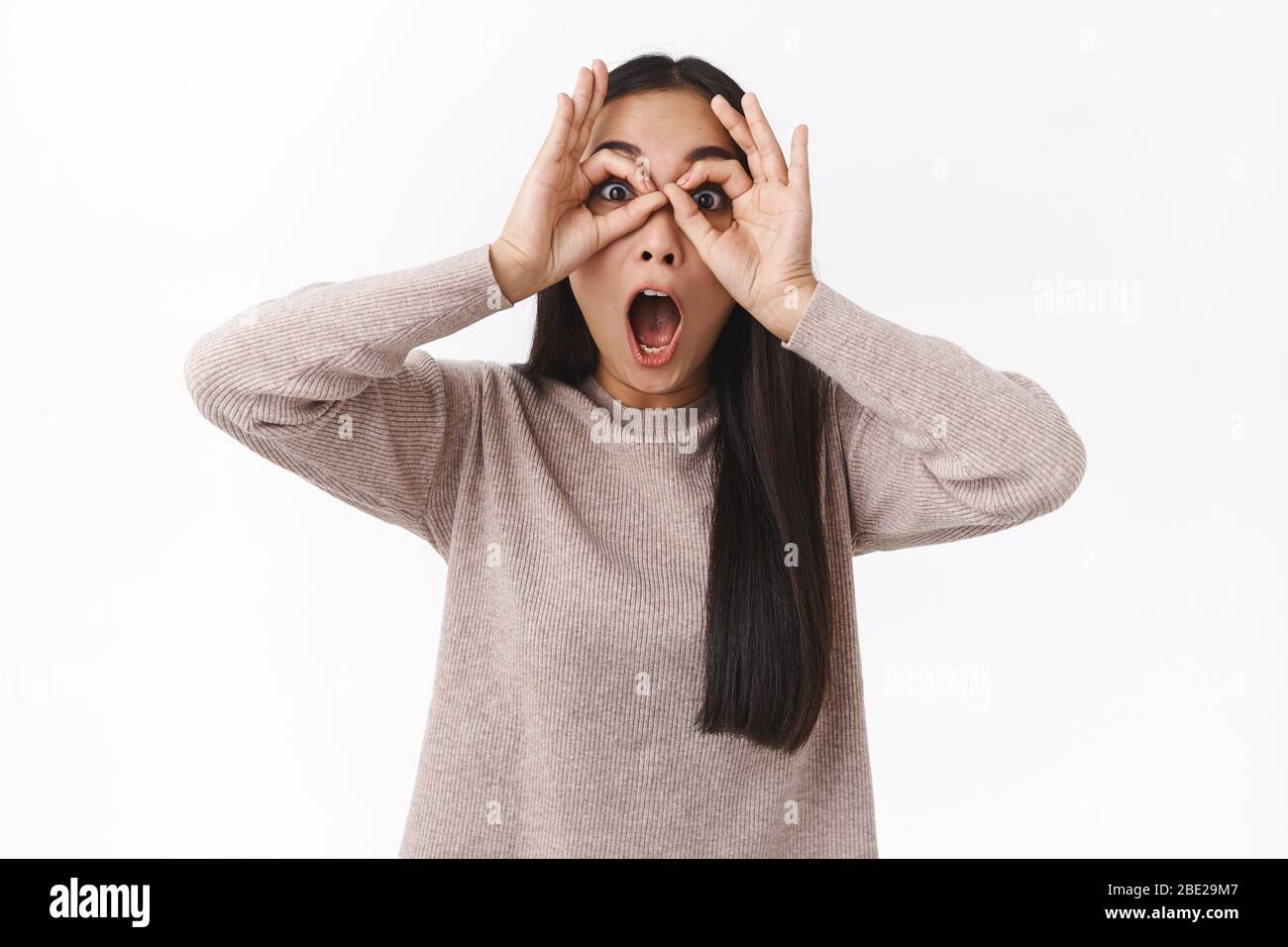 Surprised, impressed and speechless young asian girl staring mesmeriazed and excited, make finger glasses and popping eyes camera, check-out awesome Stock Photo