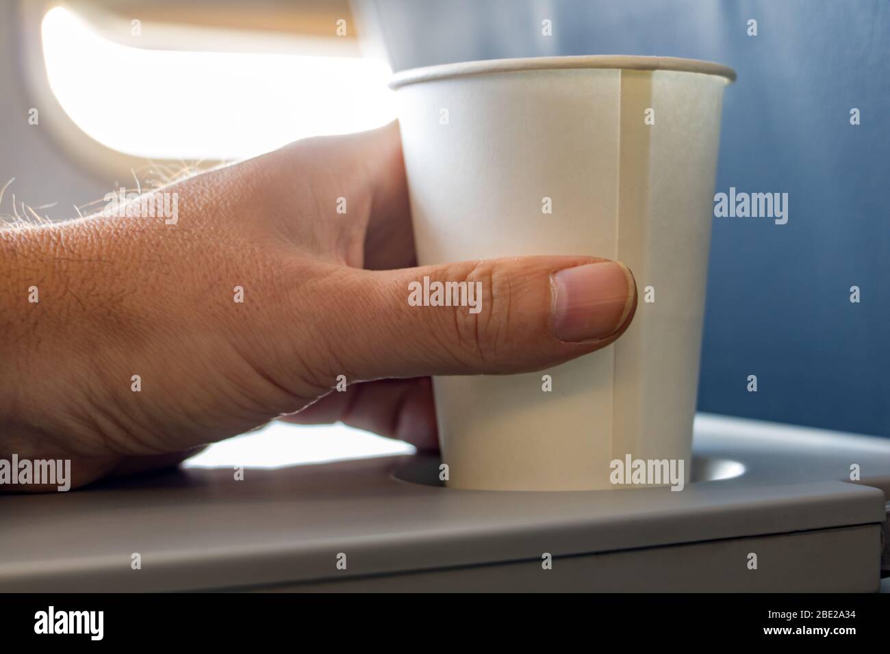 A male hand hold paper cup with drink on board in flying aircraft ...
