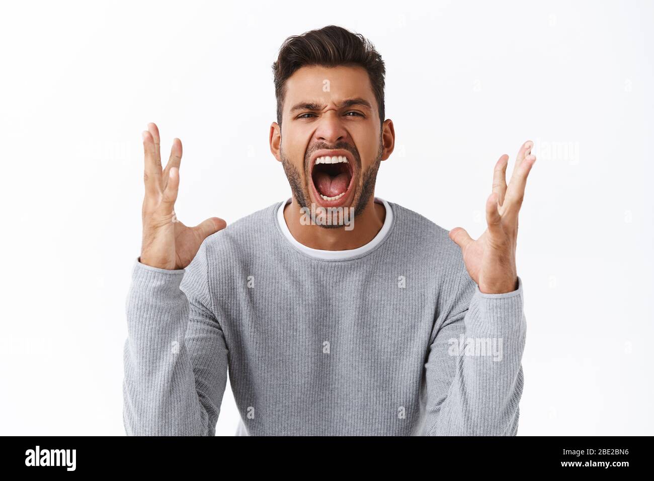 Angry and disappointed handsome bearded man in grey sweater swearing and cursing everyone as lost bid, shaking hands outraged and distressed, losing Stock Photo