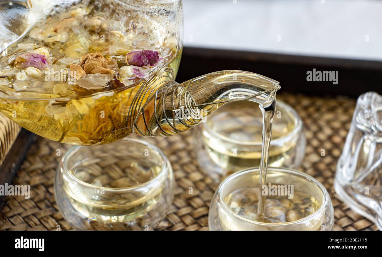 Herbal tea of drying flowers is pouring to cup, close up. A teapot and cup with flowers tea on table. Stock Photo