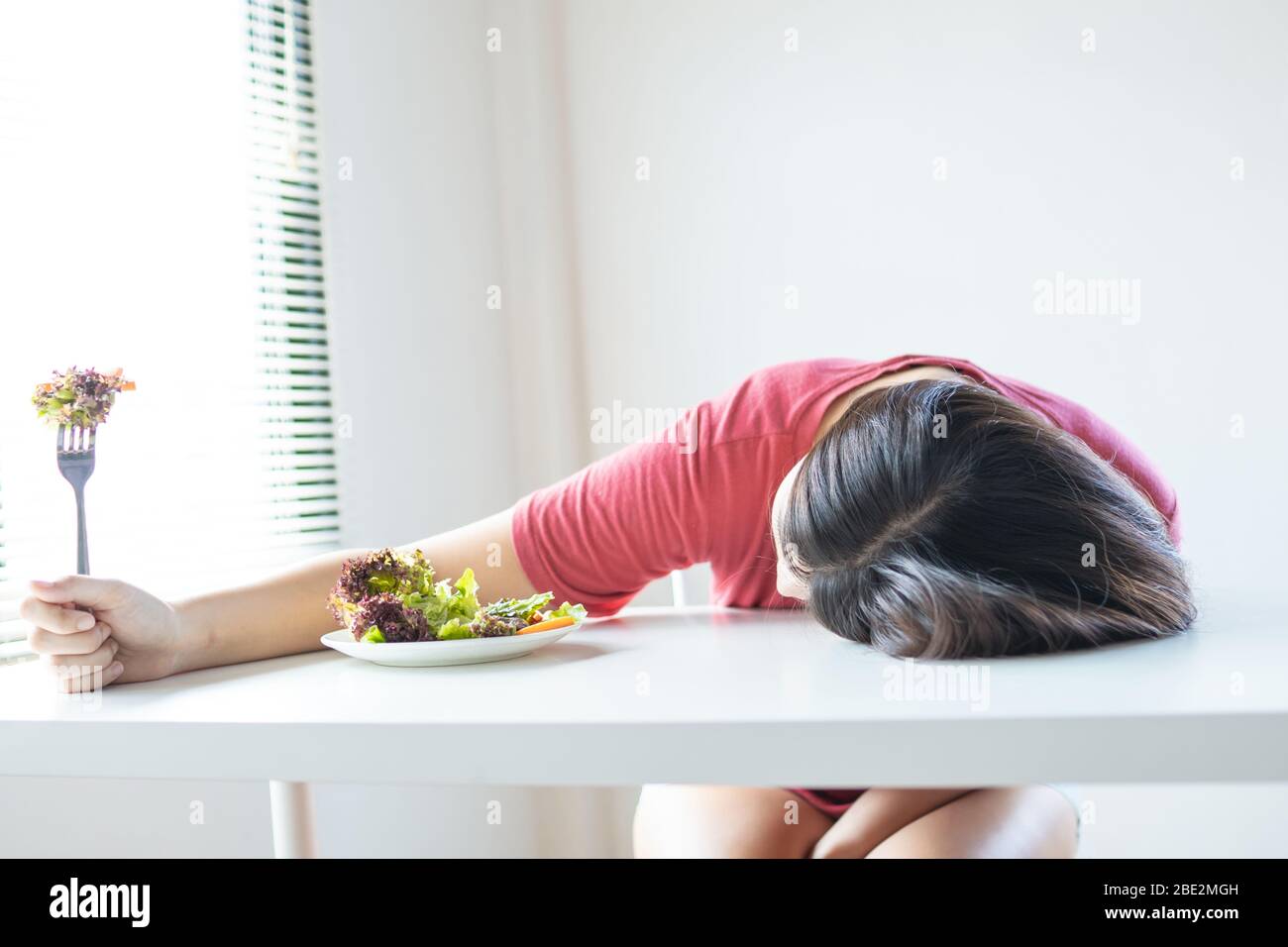 Unhappy woman bored vegetable, girl is on diet and laying down and  crouching on eating table Stock Photo