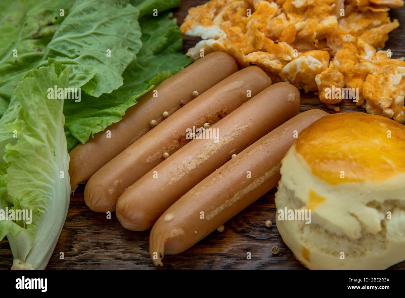 Close-up of fried sausages and scrambled eggs, scones with vegetable on wooden background. American breakfast, Selective focuse. Stock Photo
