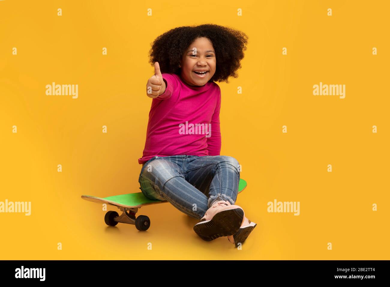 Cheerful little black girl sitting on skateboard and showing thumb up Stock  Photo - Alamy