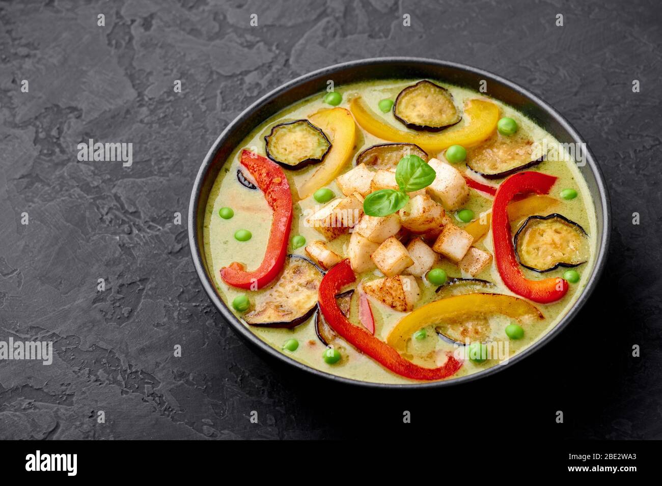 Vegetarian Thai Green Curry with tofu in black bowl at dark slate