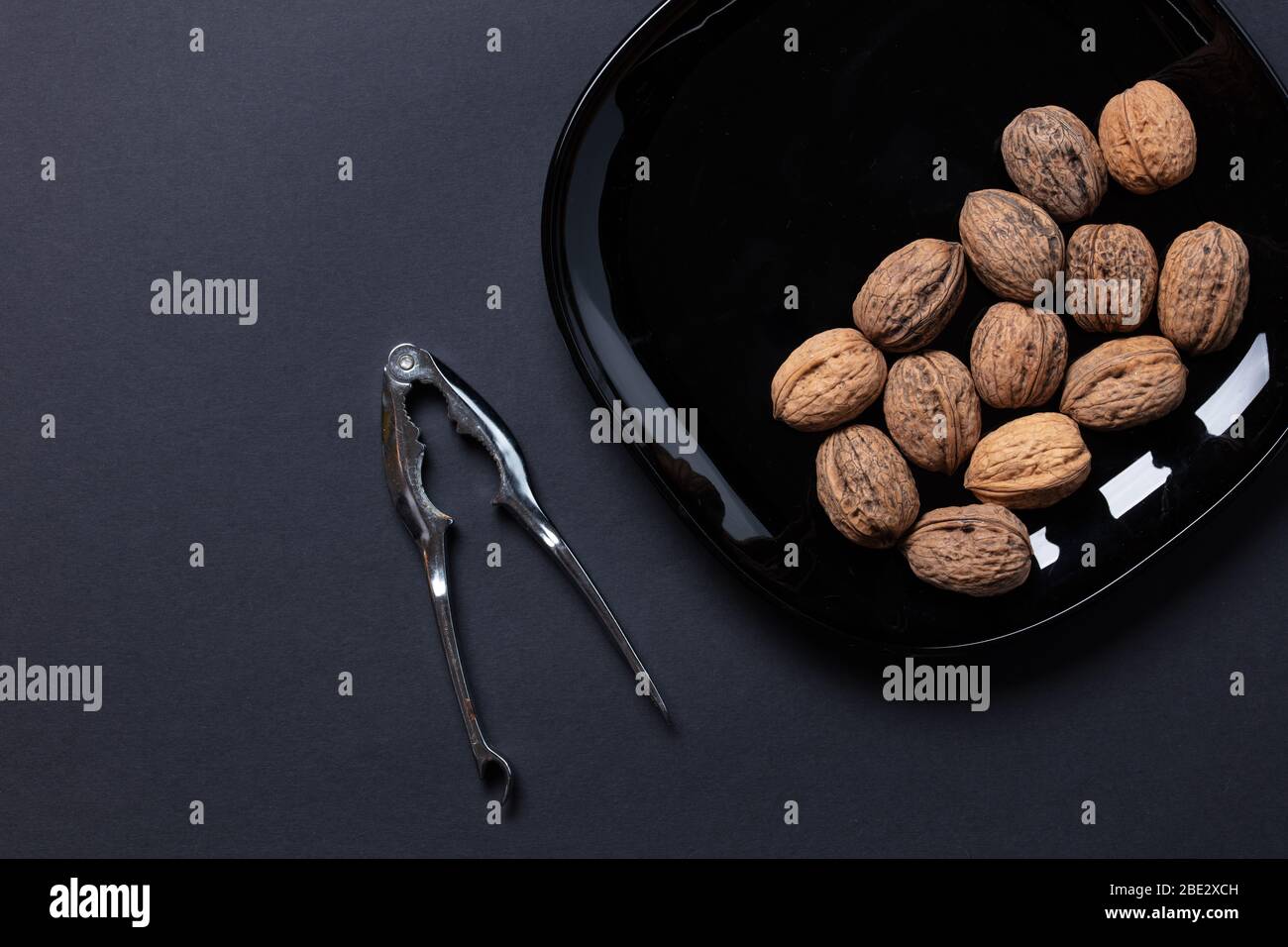 a fantastic still-life studio image of wallnuts on a black plate & nutcracker on black dark background, topview, copyspace Stock Photo