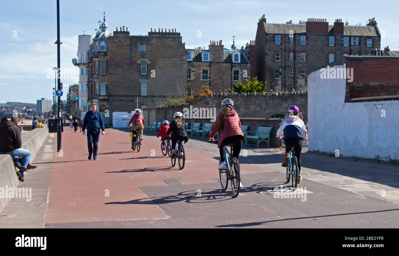 Portobello Promenade, Edinburgh, cycling Scotland, UK. 11th April 2020. Temperature of 16 degrees with full sun in the afternoon after a cloudy start. On Easter Saturday a very quiet beach on the third weekend of Coronavirus Lockdown. On the Promenade sometimes almost as many cyclists as pedestrians arriving in groups of up to five people of all ages, unfortunately not all give a physical social distance as they pass making it uncomfortable was those walking along. Credit: Arch White/ Alamy Live News. Stock Photo
