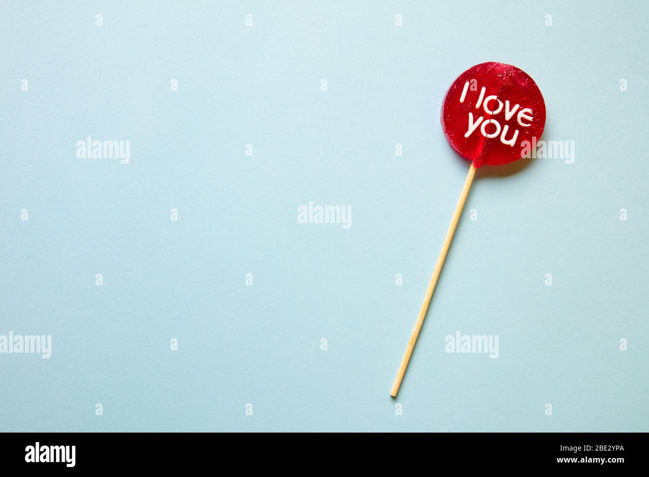 a red lollypop with 'I love you' inscription against a pastel light blue background, flat lay, top view, horizontal, conceptual Stock Photo