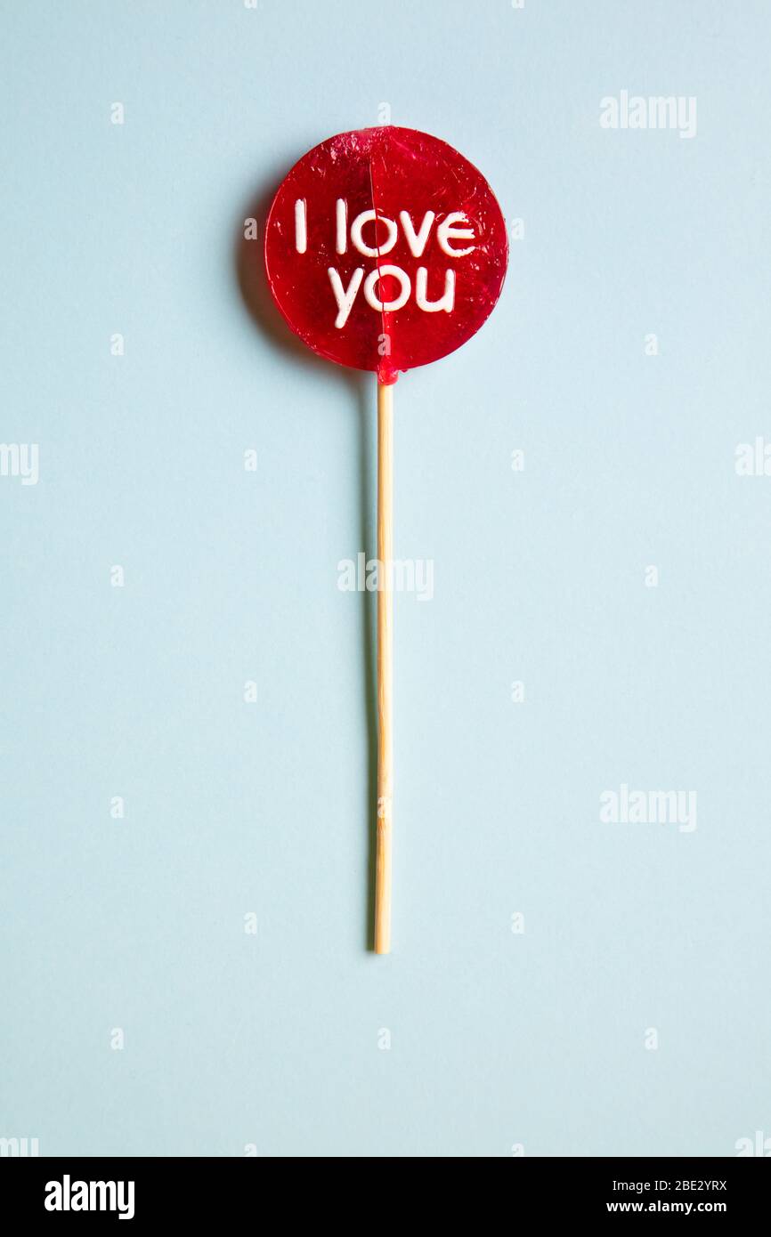 a red lollypop with 'I love you' inscription against a pastel light blue background, flat lay, top view, vertical Stock Photo