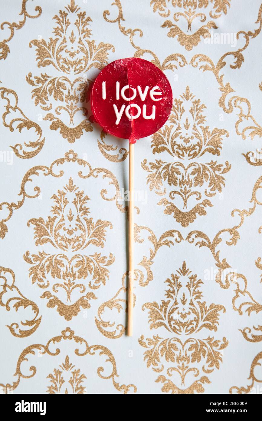a sweet 'I Love you' red lollypop against a gold and light blue decorated damask background, flat lay, top view, minimalistic, vertical Stock Photo