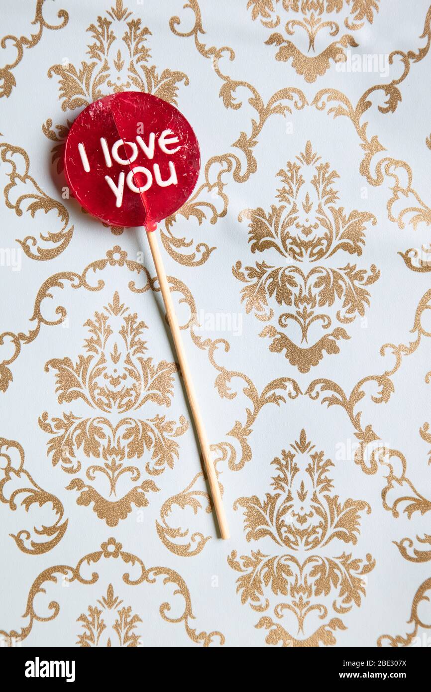 a sweet 'I Love you' red lollypop against a gold and light blue decorated background, flat lay, top view, minimalistic, vertical Stock Photo