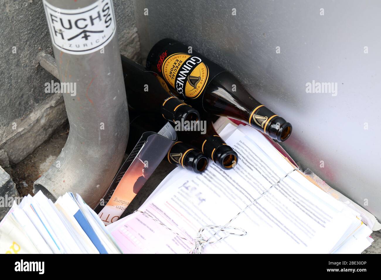 Guinness beer bottles and old papers left to a street corner near a water pipe located Zürich Switzerland, March 2020. Trash on the road to be picked. Stock Photo