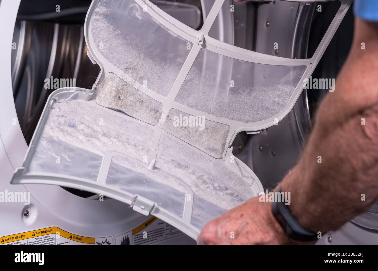 Senior caucasian man holding the lint filled trap from a front loading tumble dryer Stock Photo