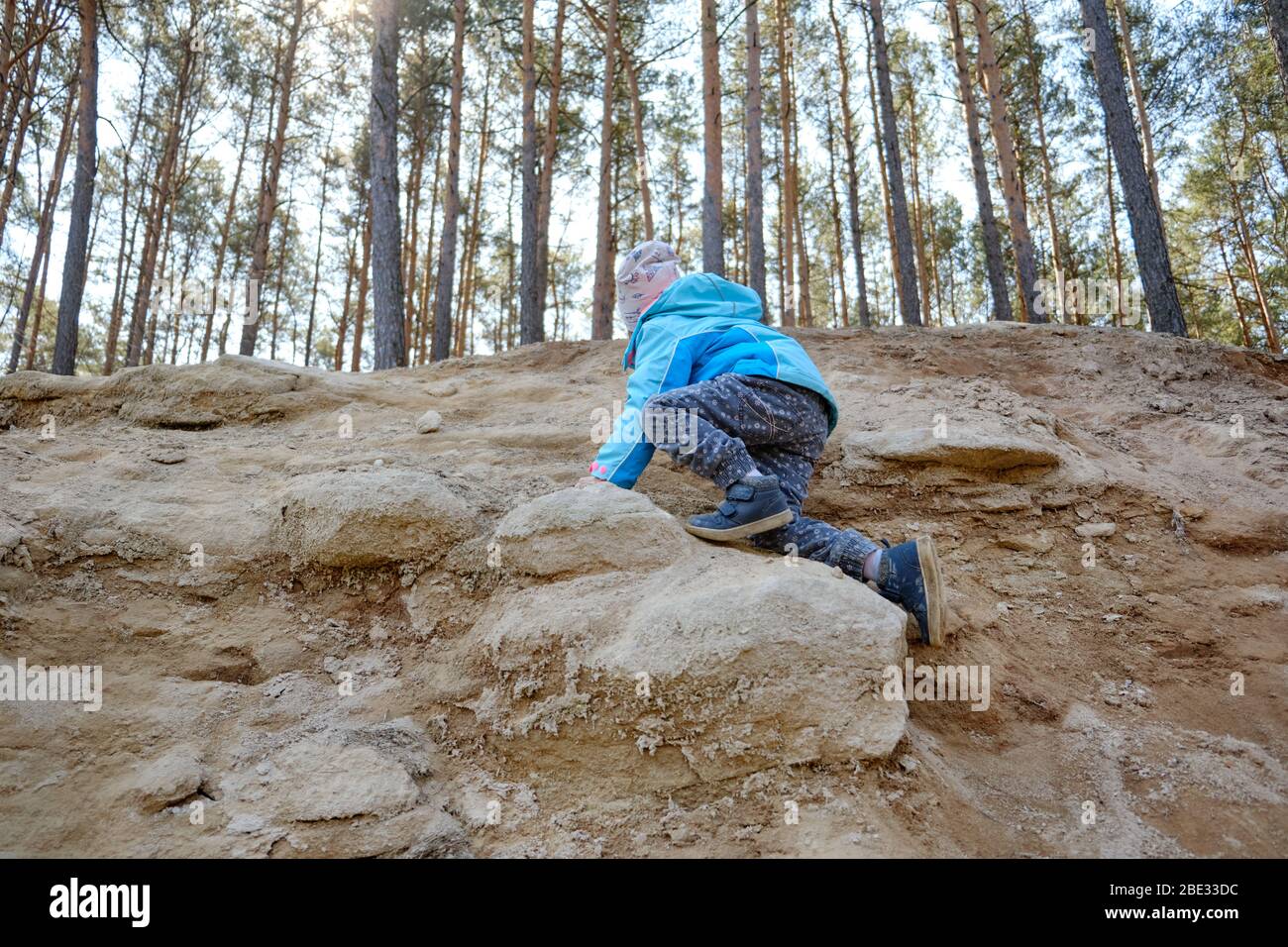 Rear view of 4 year old caucasian child girl in full length climbing up steep terrain with sandstone on a beautiful springtime day in the forest in Ge Stock Photo