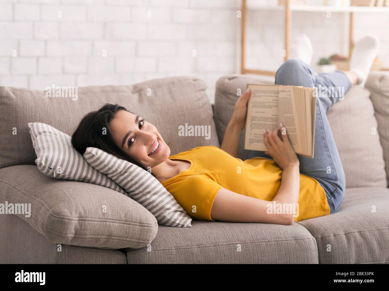 Lockdown leisure activities. Young girl reading book while lying on sofa at home Stock Photo