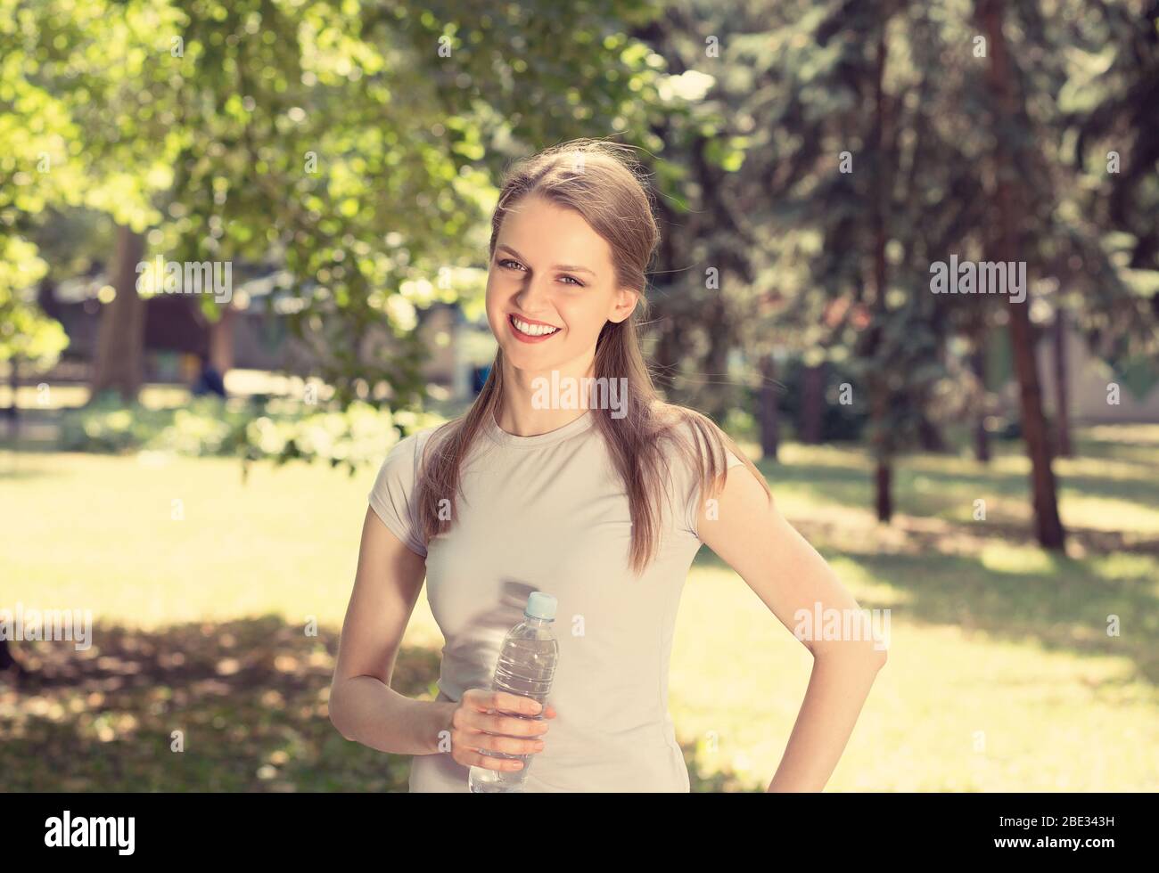 Woman holding bottle of water in hands smiling looking at you camera ...