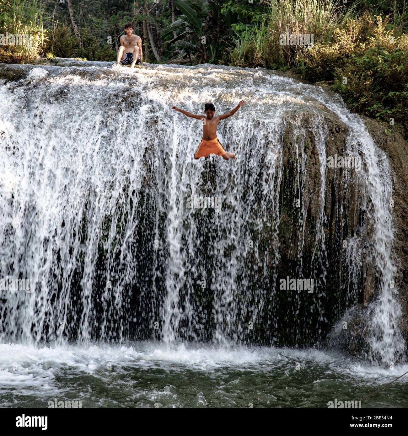 young kid diving into the river from a waterfall Stock Photo