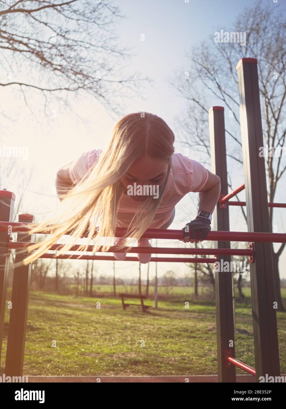 Young Athletic Woman Doing Push Ups on Monkey Bars in the Park Stock Photo